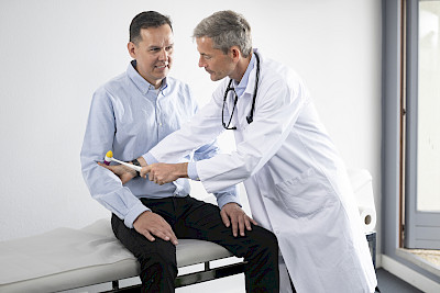 Fotografie einer Vorsorgeuntersuchung, die ein Arzt an einem Patienten durchführt